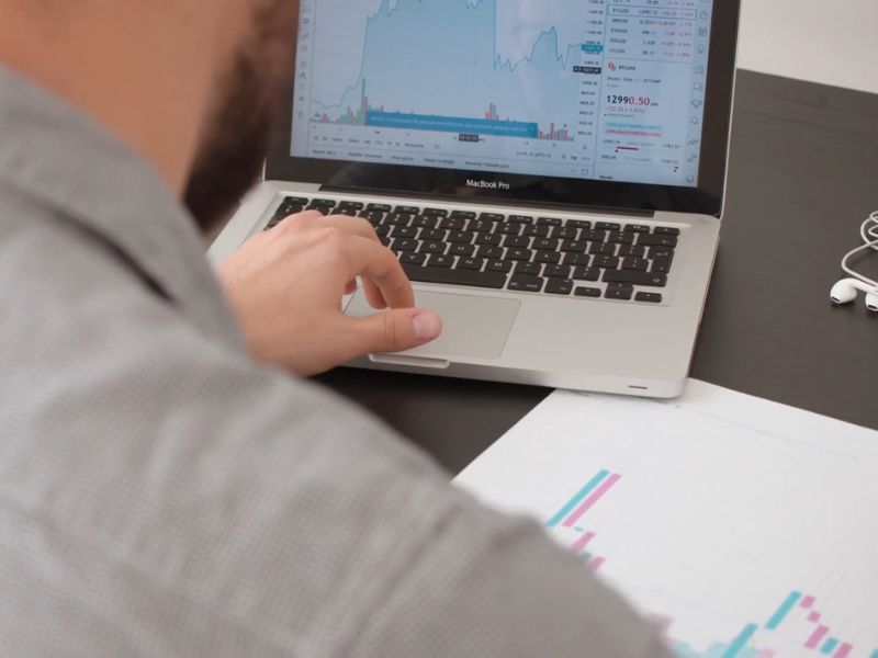 osoba unosi podatke na laptop i dopisuje nešto na papiru pored