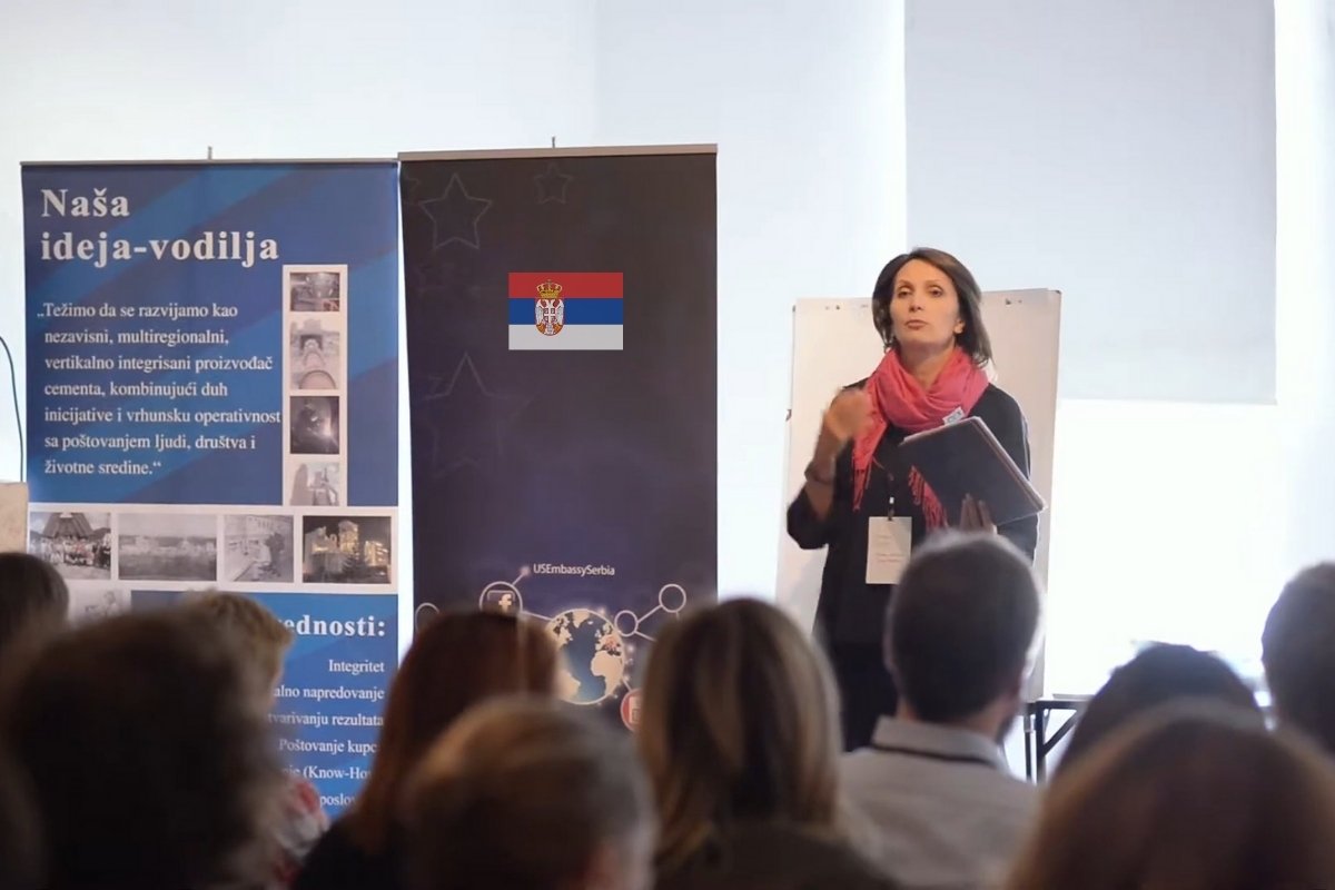 Žena drži prezentaciju pred grupom polaznika tokom edukativne radionice uz promotivne panoe u pozadini