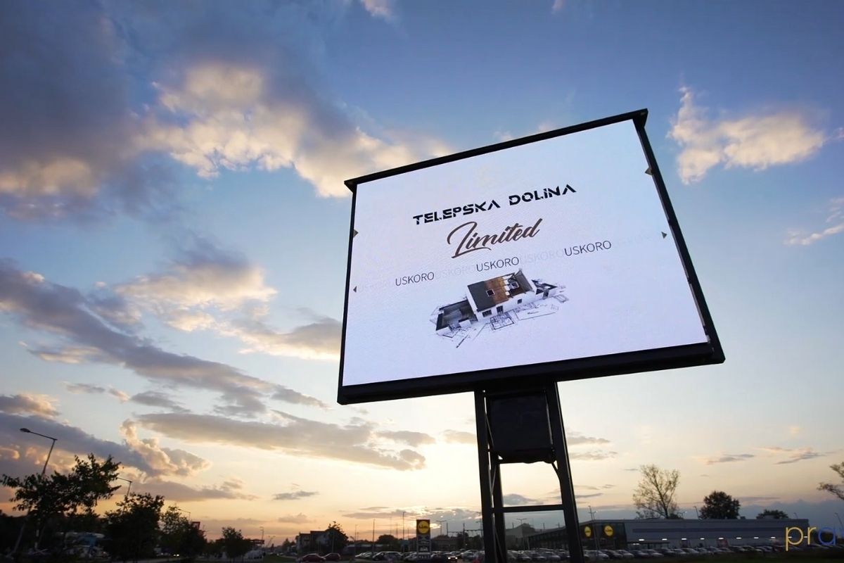 Veliki digitalni bilbord sa oglasom za stambeni kompleks, postavljen pored puta u suton